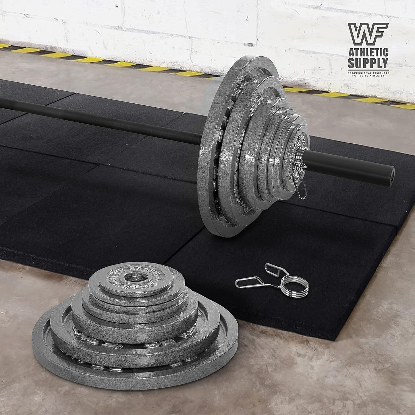 Weightlifting barbell with weight plates and clips on a black mat in a gym setting.
