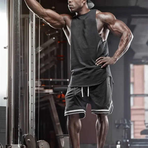 A black man working out in the gym, wearing a black mens tank top and black gym shorts sold by 100 Spartans